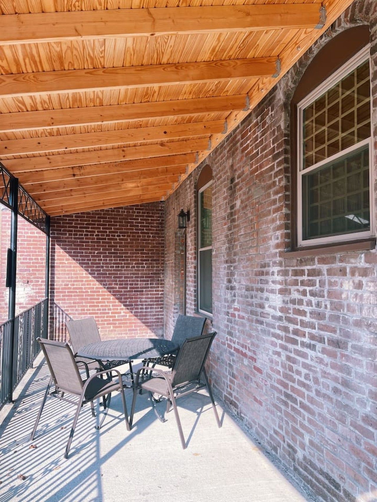 A covered patio area with a brick wall, a table with chairs, and a window.