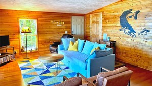 A cozy cabin interior with a blue sofa, wooden walls, a mounted fish mural, and a small round table.