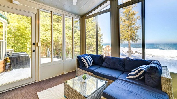 A sunroom with a large sliding glass door, a cushioned seating area, and a view of the beach.