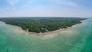 An aerial view of a coastal area with dense forest, clear turquoise waters, and a small peninsula with buildings.