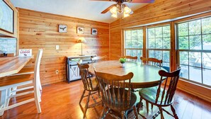 A wooden interior with a dining table, chairs, a ceiling fan, and large windows.