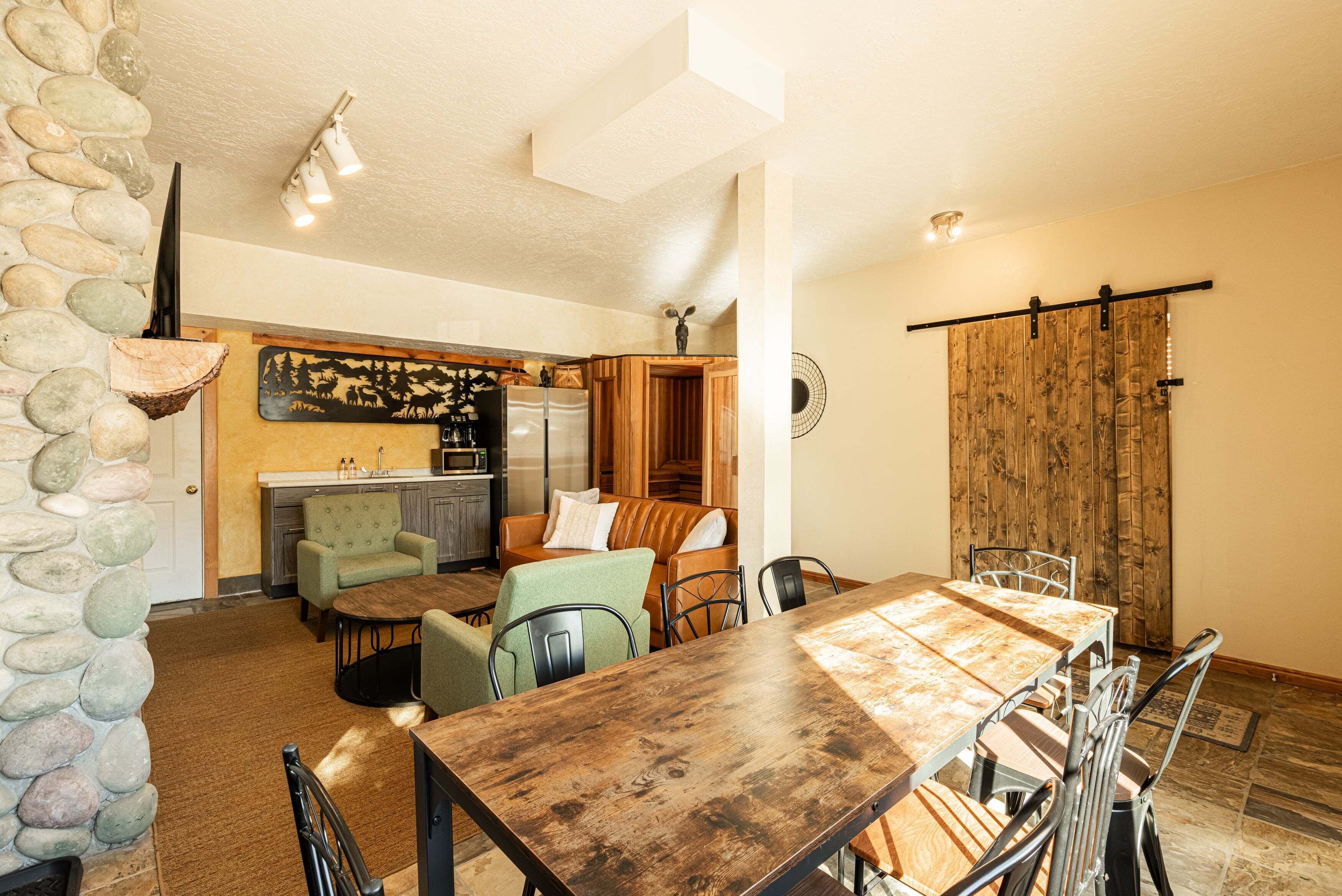 A dining area with a wooden table and chairs, a kitchen with a stone wall, and a sliding barn door.