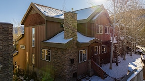 Une maison à plusieurs étages, dotée d’une façade en pierre, d’un revêtement extérieur en bois et d’un toit recouvert de neige.
