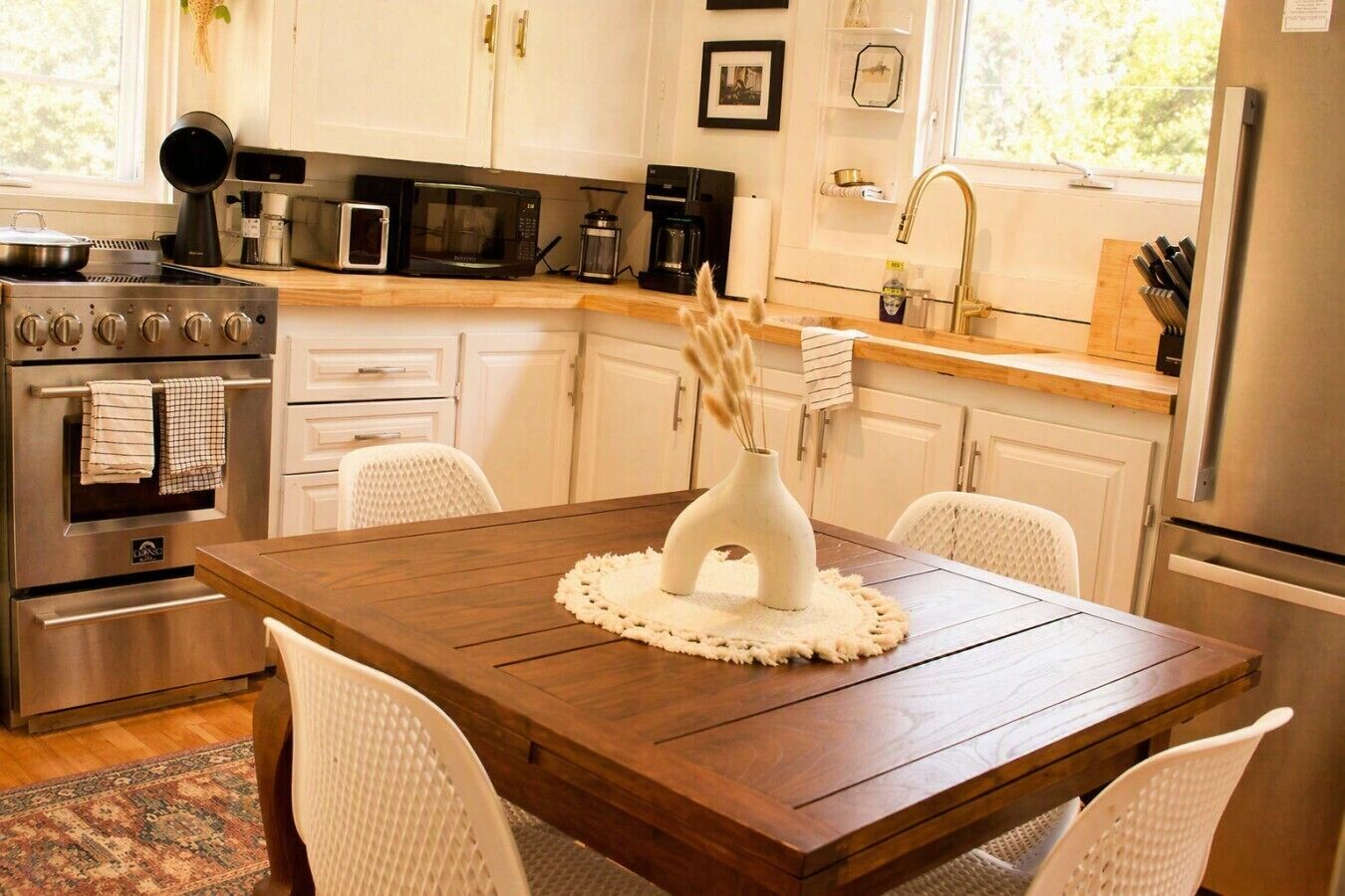 Une cuisine moderne avec des meubles blancs, des appareils en acier inoxydable et une table à manger en bois, assortie de chaises blanches.