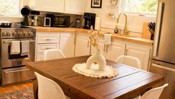 Une cuisine moderne avec des meubles blancs, des appareils en acier inoxydable et une table à manger en bois, assortie de chaises blanches.