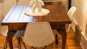 Cuina compacta amb taula de fusta, cadires blanques, nevera d'acer inoxidable i finestra amb llum natural.