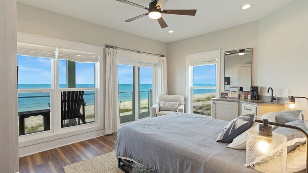 A bedroom with a bed, a ceiling fan, a nightstand, a chair, and a view of the ocean. - Oak Rest Barn, is a custom built gulf front home w/pool, pet friendly, $250 credit for beach gear! (Port Saint Joe)