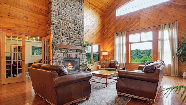Ein gemütliches Wohnzimmer mit Kamin aus Stein, Ledersofas und großen Fenstern mit Blick ins Freie.
