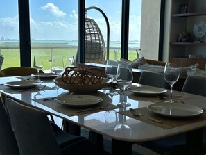A dining table set for two with a view of the sea and a beach.