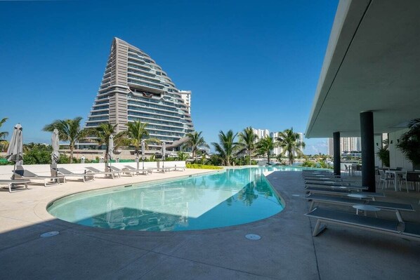 A modern hotel with a pool area, lounge chairs, and palm trees.