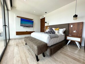 A modern bedroom with a large bed, a TV mounted on the wall, and a wooden wardrobe.