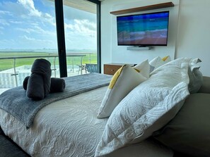 A hotel room with a large bed, a television mounted on the wall, and a balcony with a view of the landscape.