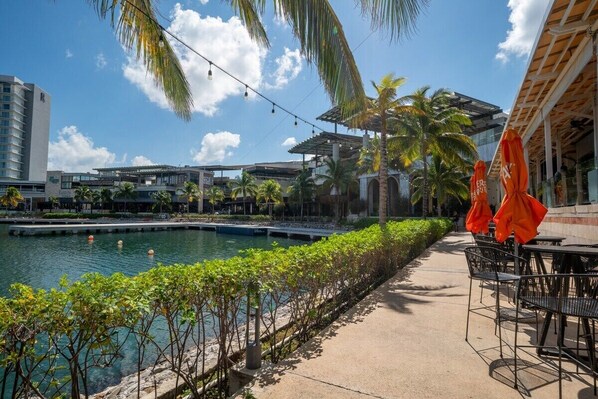 A poolside area with outdoor seating, palm trees, and a view of a hotel building.