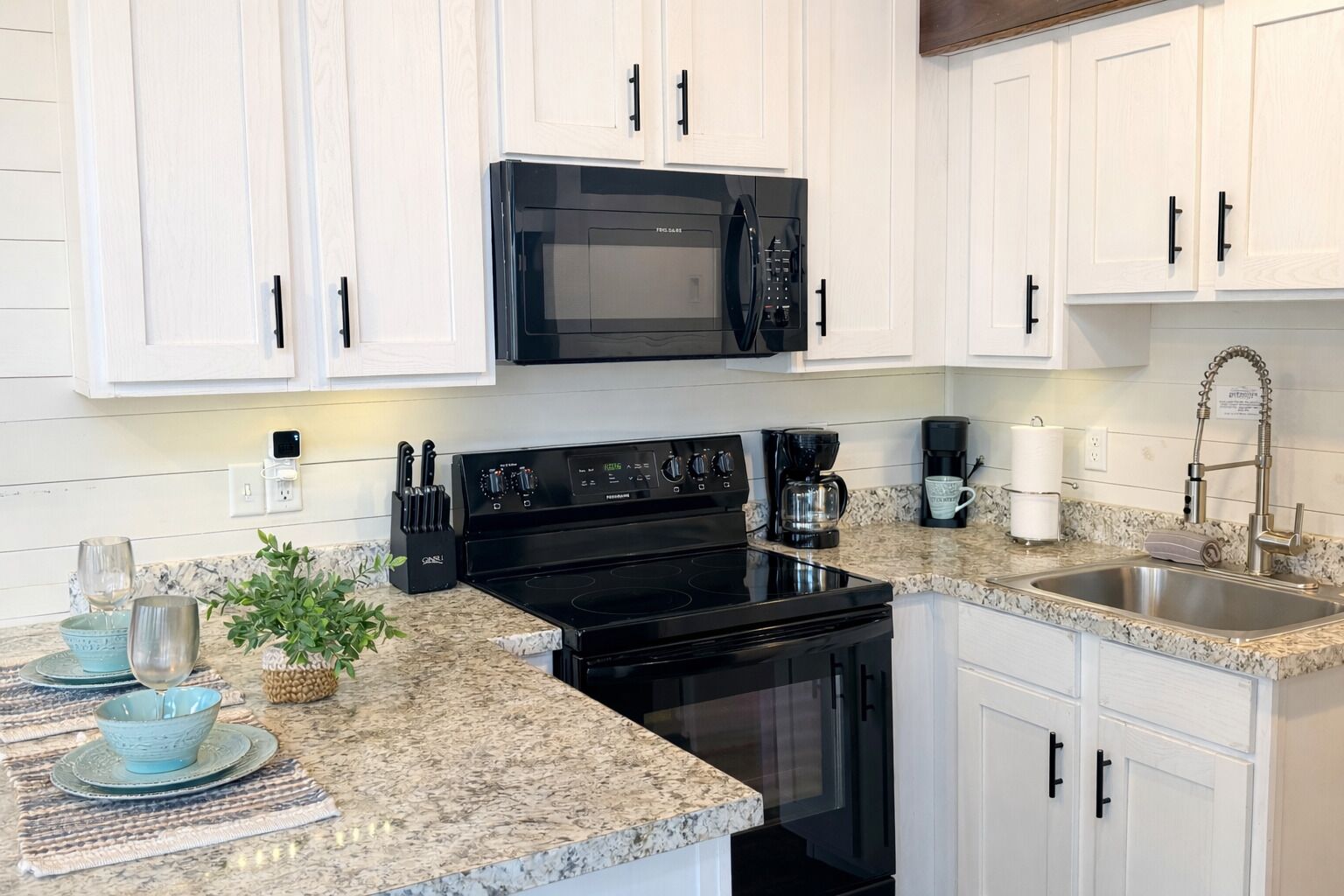 A modern kitchen with white cabinets, a black microwave, a stove, and a stainless steel sink.