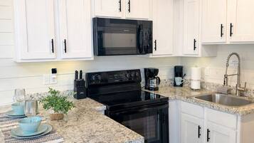 A modern kitchen with white cabinets, a black microwave, a stove, and a stainless steel sink.