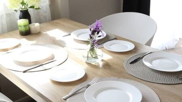 Una mesa de comedor preparada con platos, cubiertos y manteles individuales.