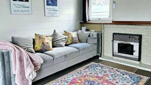 Una sala de estar con un sofá, almohadones coloridos, una chimenea y dos cuadros en la pared.