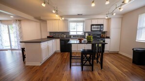 A modern kitchen with white cabinets, a central island, and a black countertop. - Vacation home, < 1 mile to University of Notre Dame, walk, bike or drive! (South Bend)