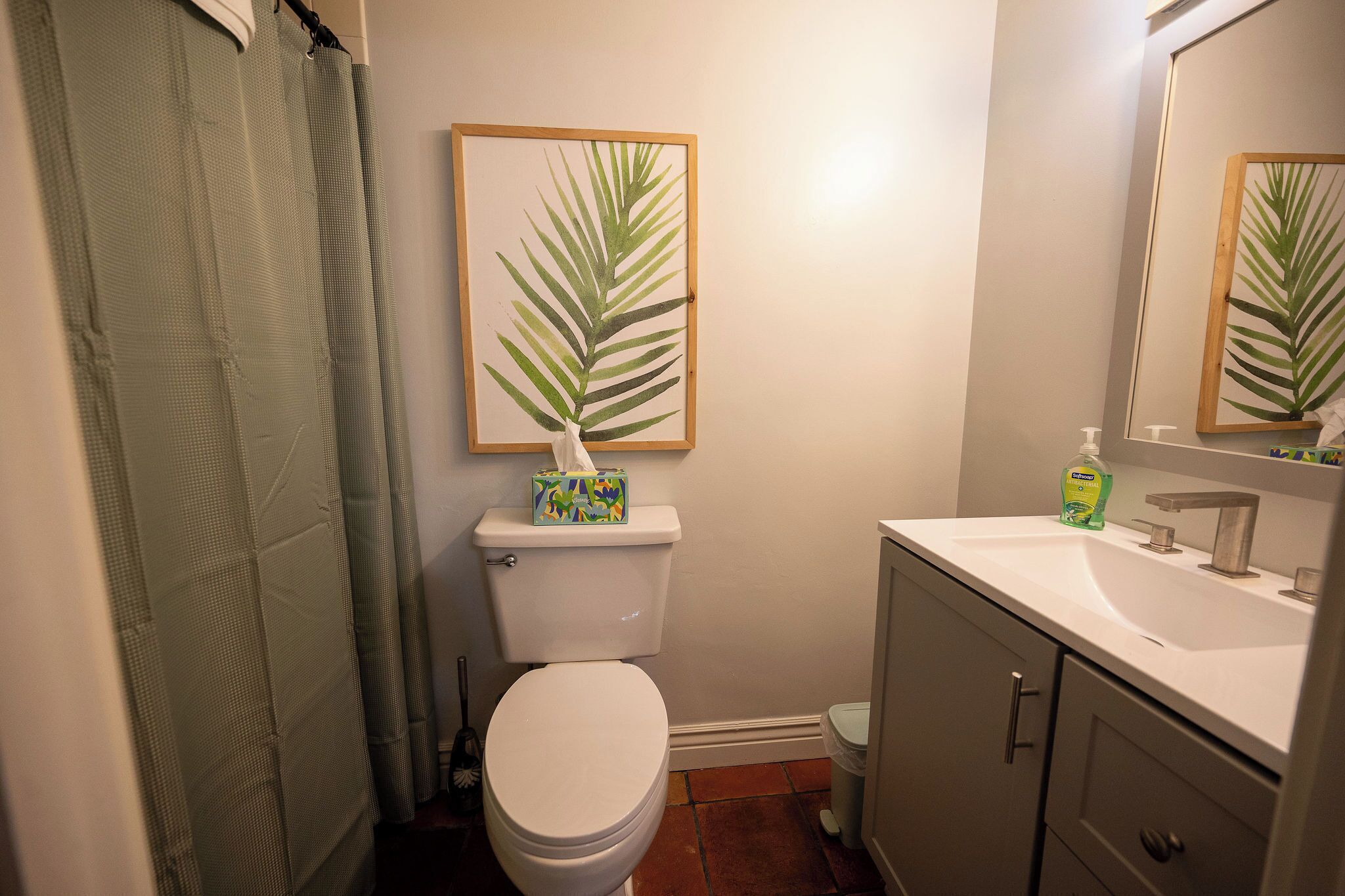 A bathroom with a toilet, sink, and a framed plant on the wall.