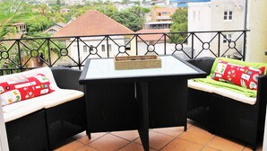 Un balcon avec une table et deux canapés en osier, l’un avec un coussin rouge et l’autre avec un coussin vert.