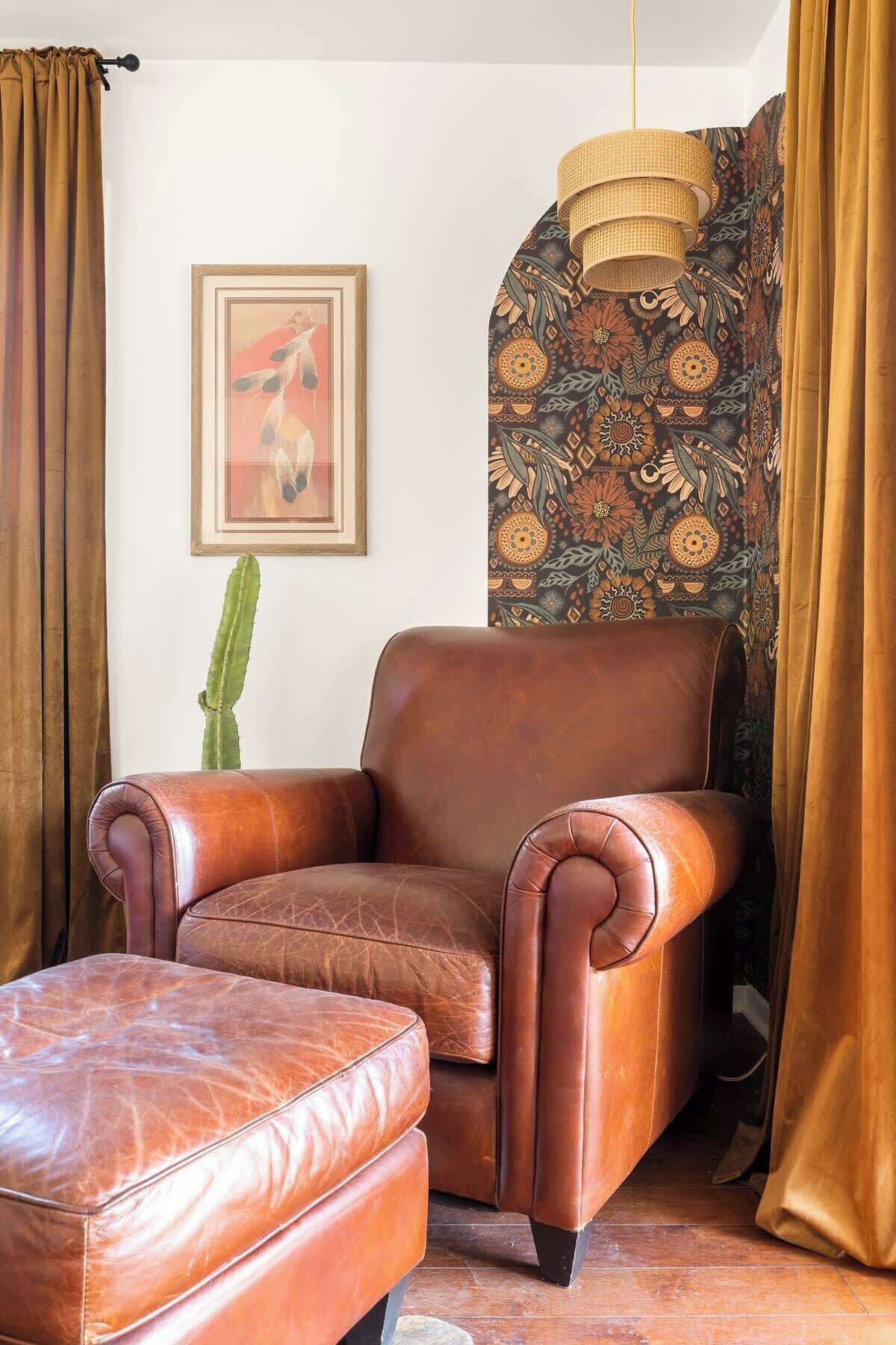 A leather armchair with a matching ottoman, a cactus plant, a framed artwork, and patterned curtains.