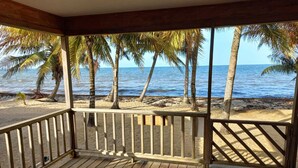 Una terraza de madera con vista a la playa y palmeras.