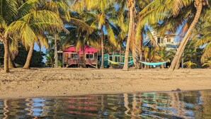 Una playa con palmeras, una hamaca y un edificio rosa con balcón.