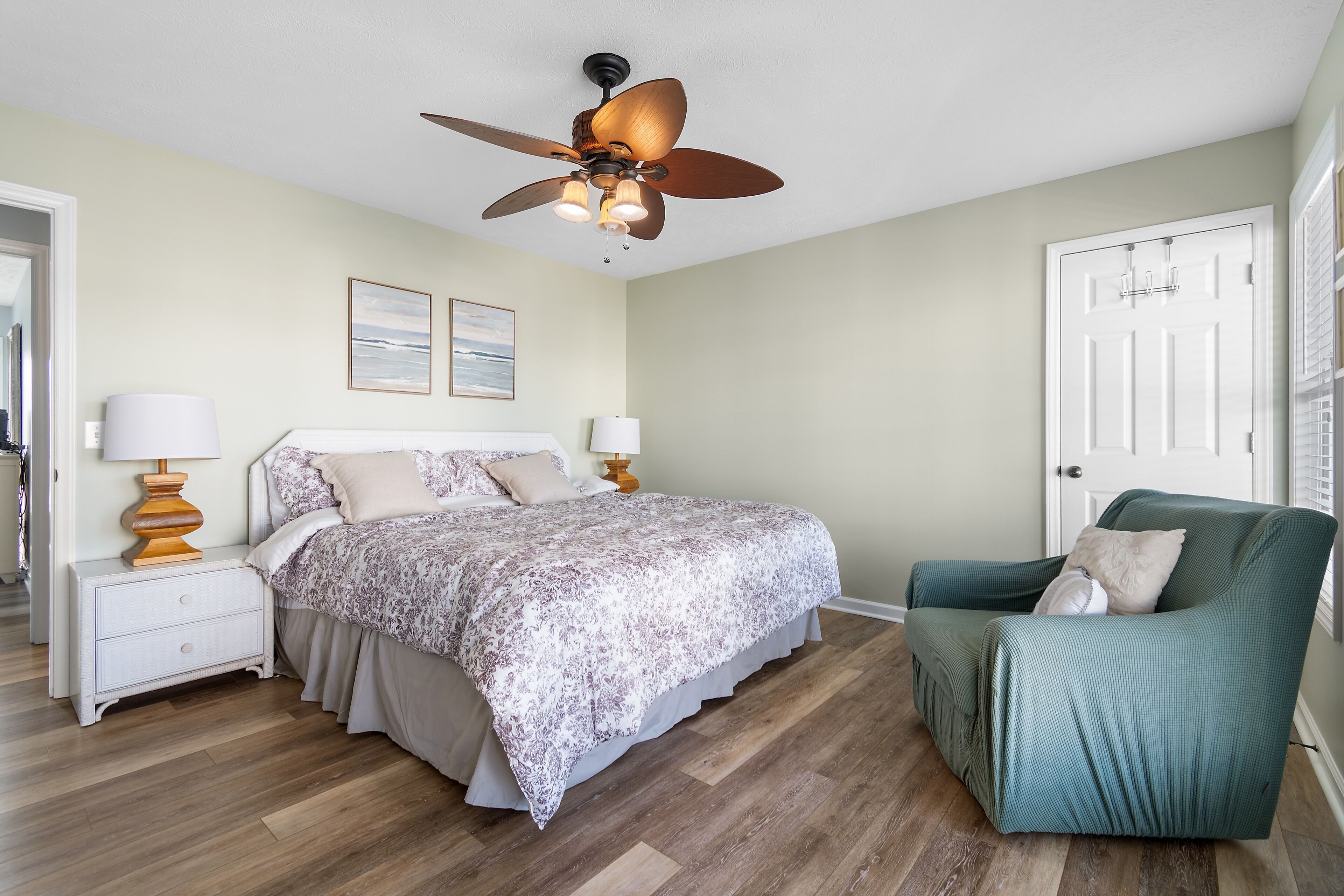 A bedroom with a bed, nightstands, a green armchair, a ceiling fan, and a door.