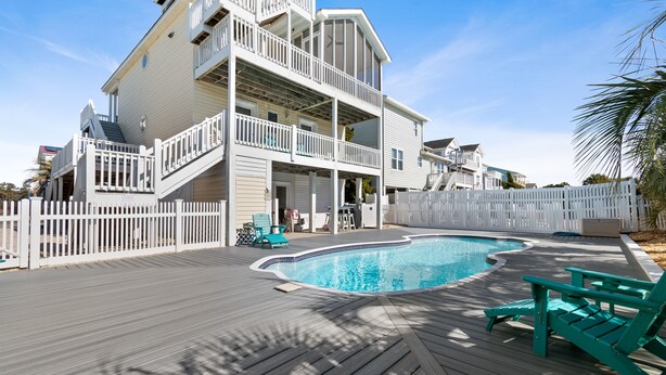 A two-story building with a swimming pool and deck chairs.