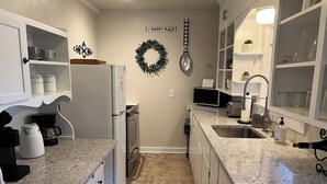 Cocina compacta con armarios blancos, encimeras de granito, cafetera, microondas y lavabo.