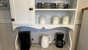 Una cocina con encimera de granito, un armario blanco con repisa superior y una cafetera sobre la encimera.