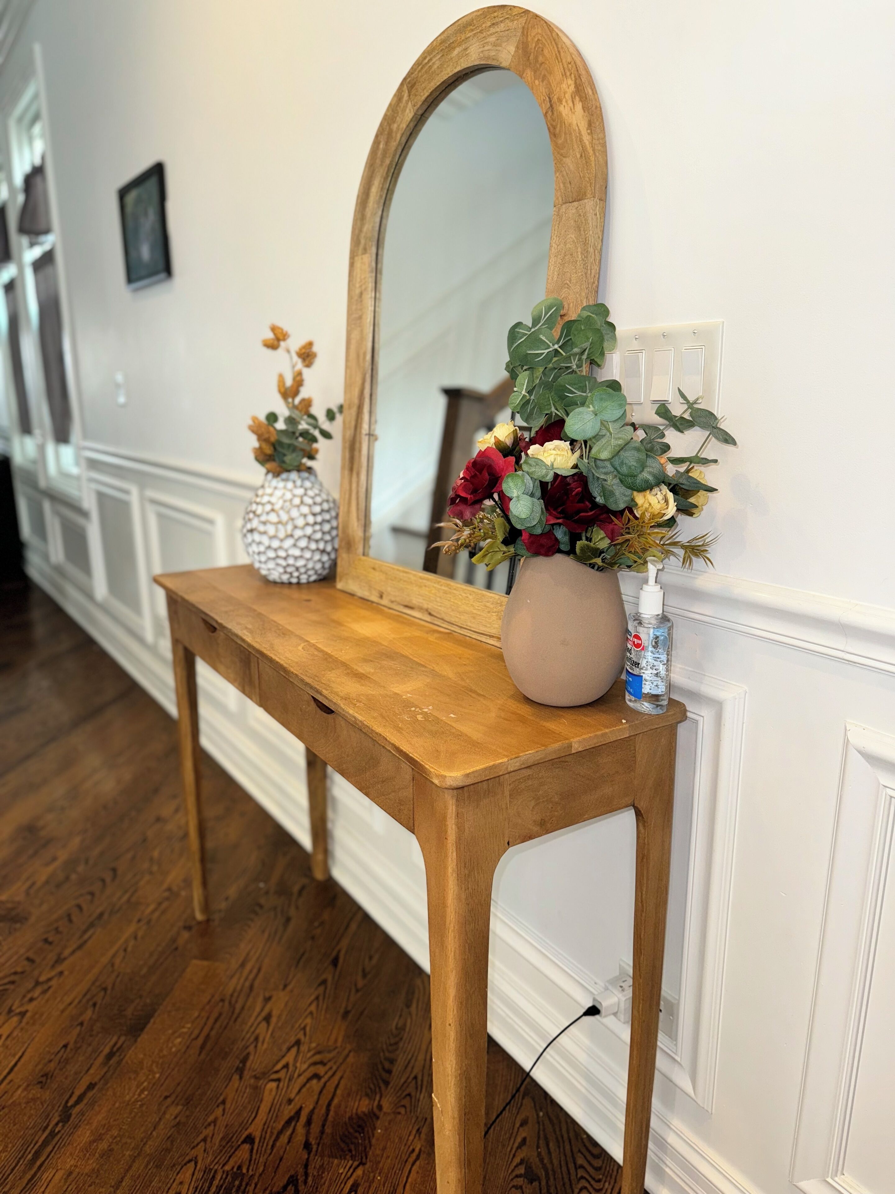 Une console en bois, agrémentée d’un miroir et de deux vases de fleurs.