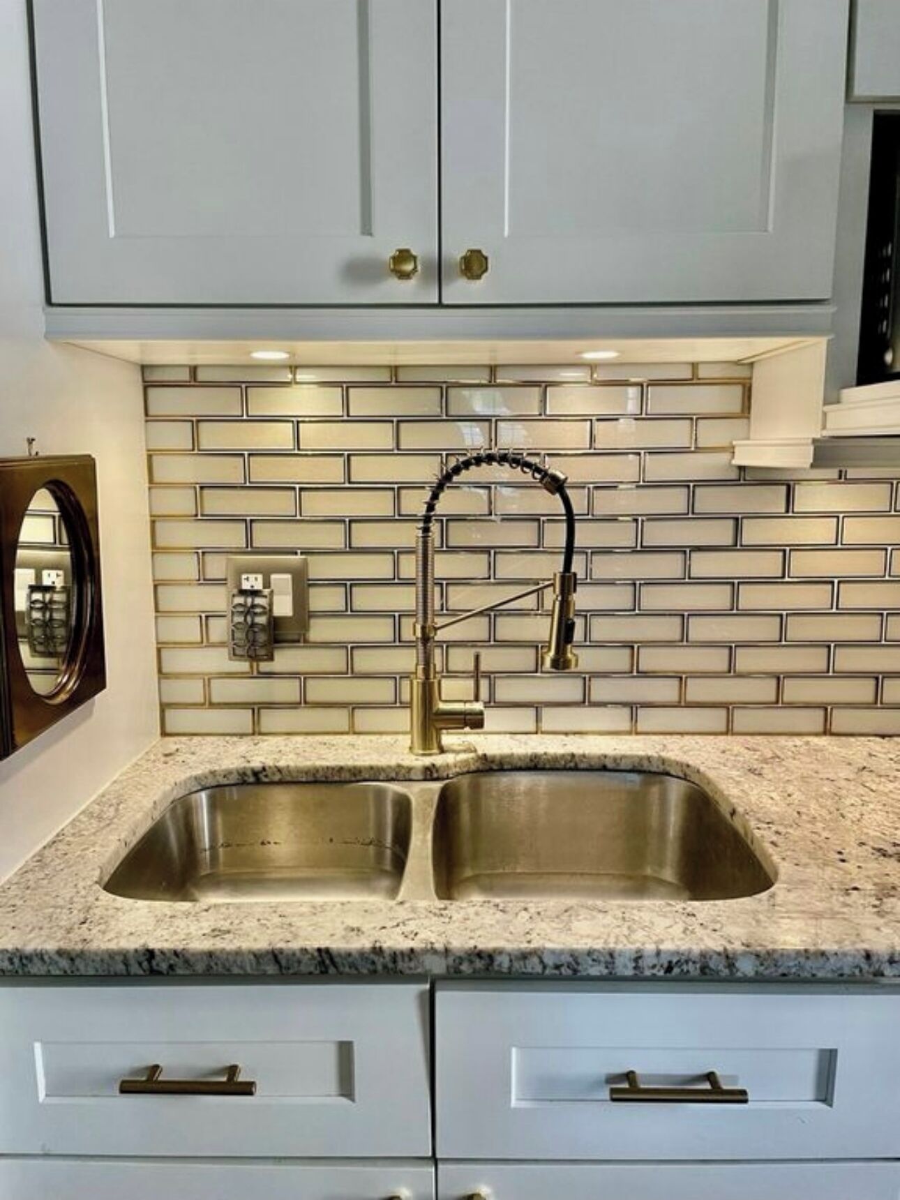 Una cocina con armarios blancos, un lavamanos doble y un salpicadero con azulejos blancos.
