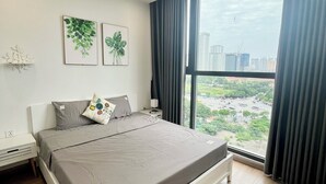 Ett modernt sovrum med en stor säng, ett nattduksbord, en väggmonterad ventilationsöppning och ett fönster med gardiner.