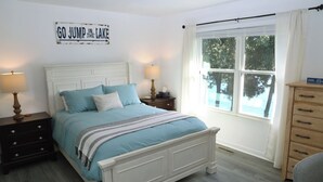 A bedroom with a bed, nightstands, a dresser, and a window with a view of trees. - Waterfront Townhome- with Boat Slip and Dock! (Moneta)
