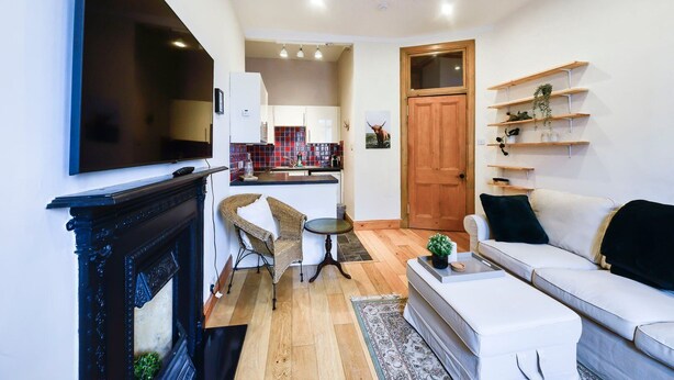 A compact living space with a fireplace, a sofa, a dining area, and a kitchen in the background. - GuestReady - Comfortable 1Bed in Leith (Edinburgh)