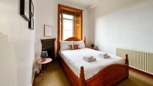 A bedroom with a wooden bed, a small table with a lamp, a fireplace, and a radiator. - GuestReady - Comfortable 1Bed in Leith (Edinburgh)