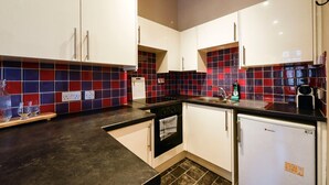 A modern kitchen with white cabinets, a black countertop, and red and blue tiles on the backsplash. - GuestReady - Comfortable 1Bed in Leith (Edinburgh)