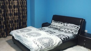 A bedroom with a bed, a nightstand, a green fan, and patterned curtains. - KalBock Apartment  (Monrovia)