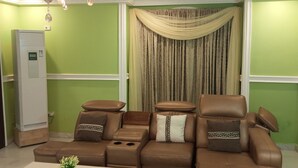 A living room with a brown leather sofa set, a white air conditioning unit, and a decorative curtain. - KalBock Apartment  (Monrovia)