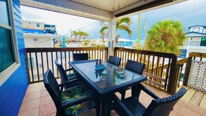 A covered outdoor area with a table and chairs, a ceiling fan, and a view of buildings and palm trees.