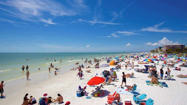 A crowded beach with people sunbathing and swimming.