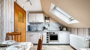 Une cuisine dotée d’une lucarne, de meubles blancs, d’un four encastré et d’un coin repas avec une table dressée pour deux personnes.