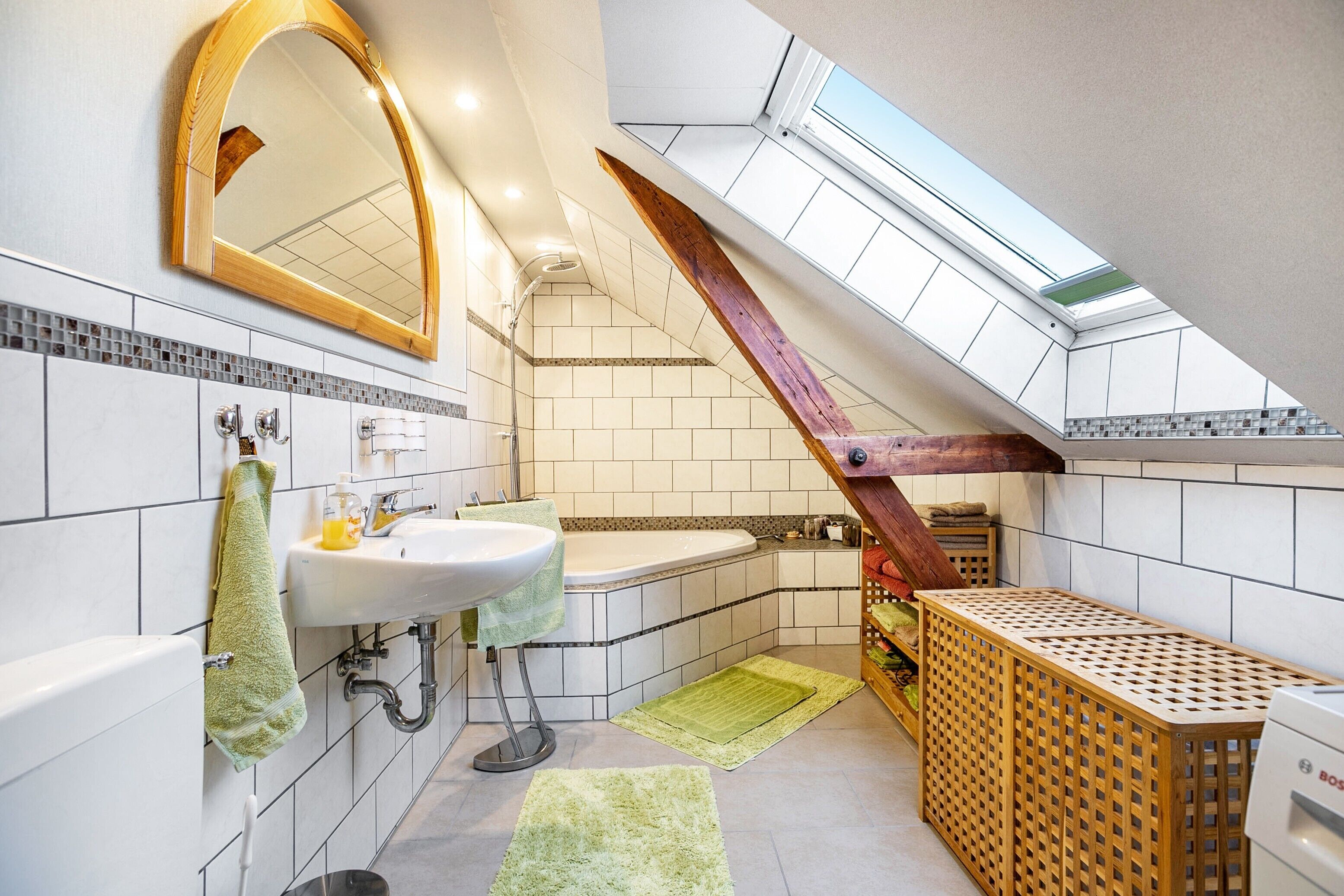 A modern bathroom with a skylight, a wooden staircase, a sink, and a bathtub.