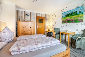 Ein Zimmer mit einem Bett, einem Holzschrank, Korbstühlen, einem Tisch und einem Bild an der Wand.