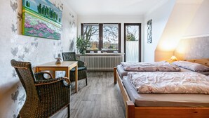 Une chambre à coucher comprenant un lit, un bureau, une chaise, un radiateur et de grandes fenêtres.