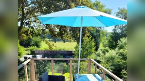 Un espace extérieur aménagé, abrité et doté de mobilier en osier et d’un parasol bleu.