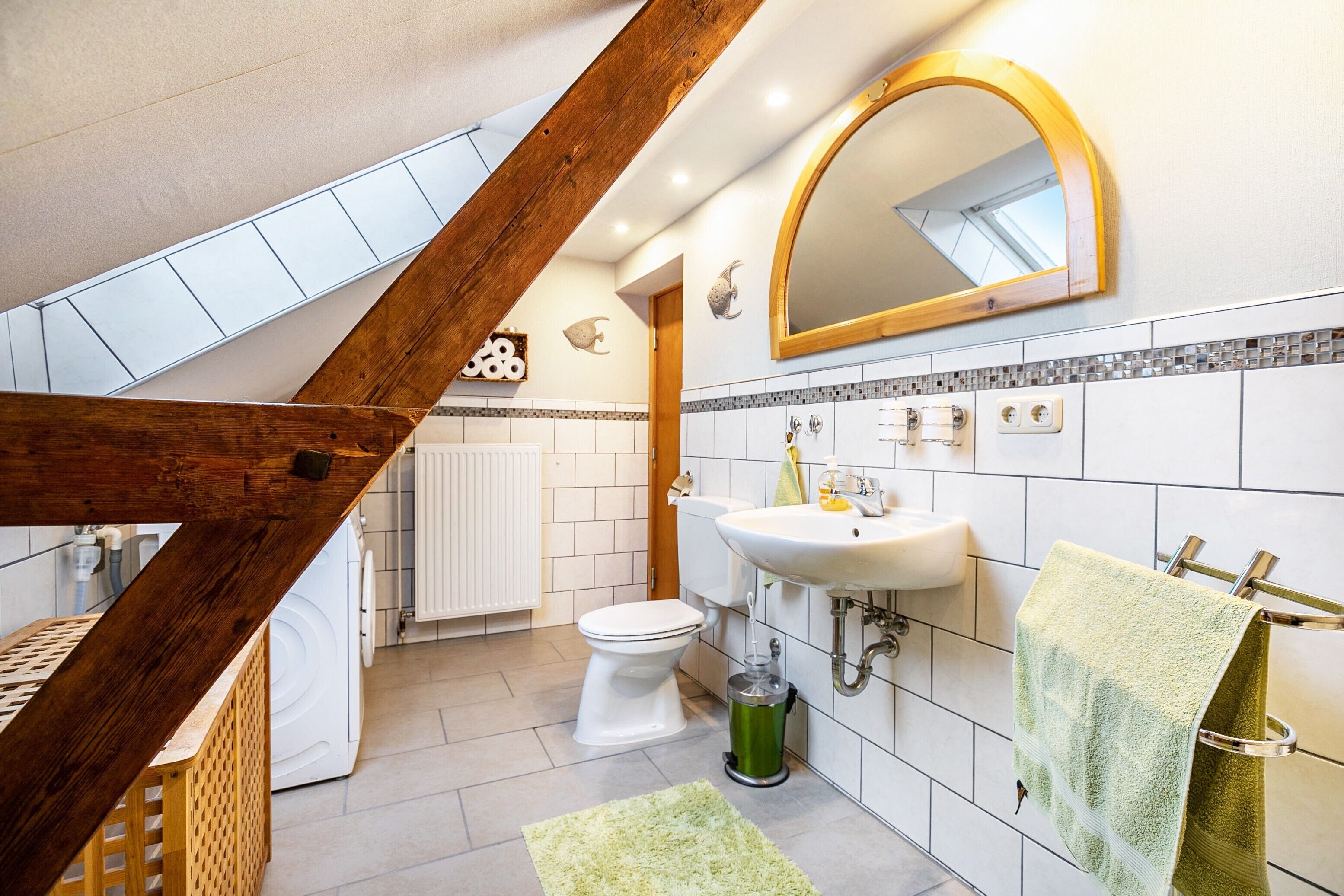 A bathroom with a white toilet, a sink, a mirror, and a green trash bin.