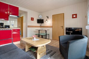 A compact living space with a kitchenette, a dining table, a sofa, and a television.