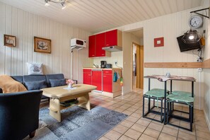 A compact living space with a sofa, a dining table, a kitchen area with red cabinets, and a small table with chairs.
